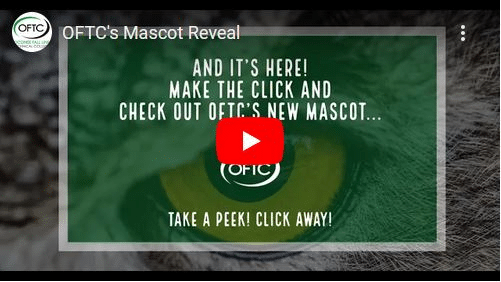 The image shows a YouTube video thumbnail with text: And it's here! Make the click and check out OFTC’s new mascot… Take a peek! Click away! The background has an animal eye, and the OFTC logo is in the center.