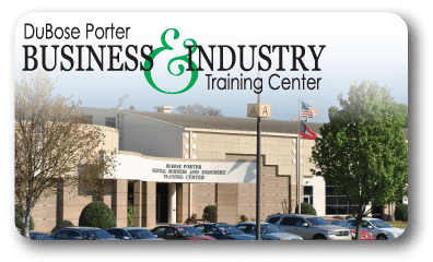 Exterior of the DuBose Porter Business and Industry Training Center with clear building signage, trees, parked cars, and two flags on flagpoles in front of the entrance.