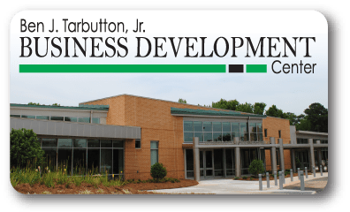A modern brick building with large glass windows labeled Ben J. Tarbutton, Jr. Business Development Center on a sign above the entrance, with landscaping and trees in the background.