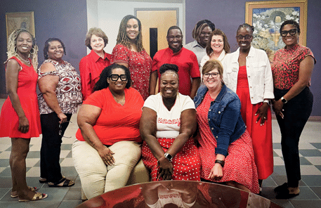 Twelve adults of from OFTC's Student Affairs Department smile while posing together indoors. Most are dressed in red or white clothing. Some stand at the back, while others sit in front. 