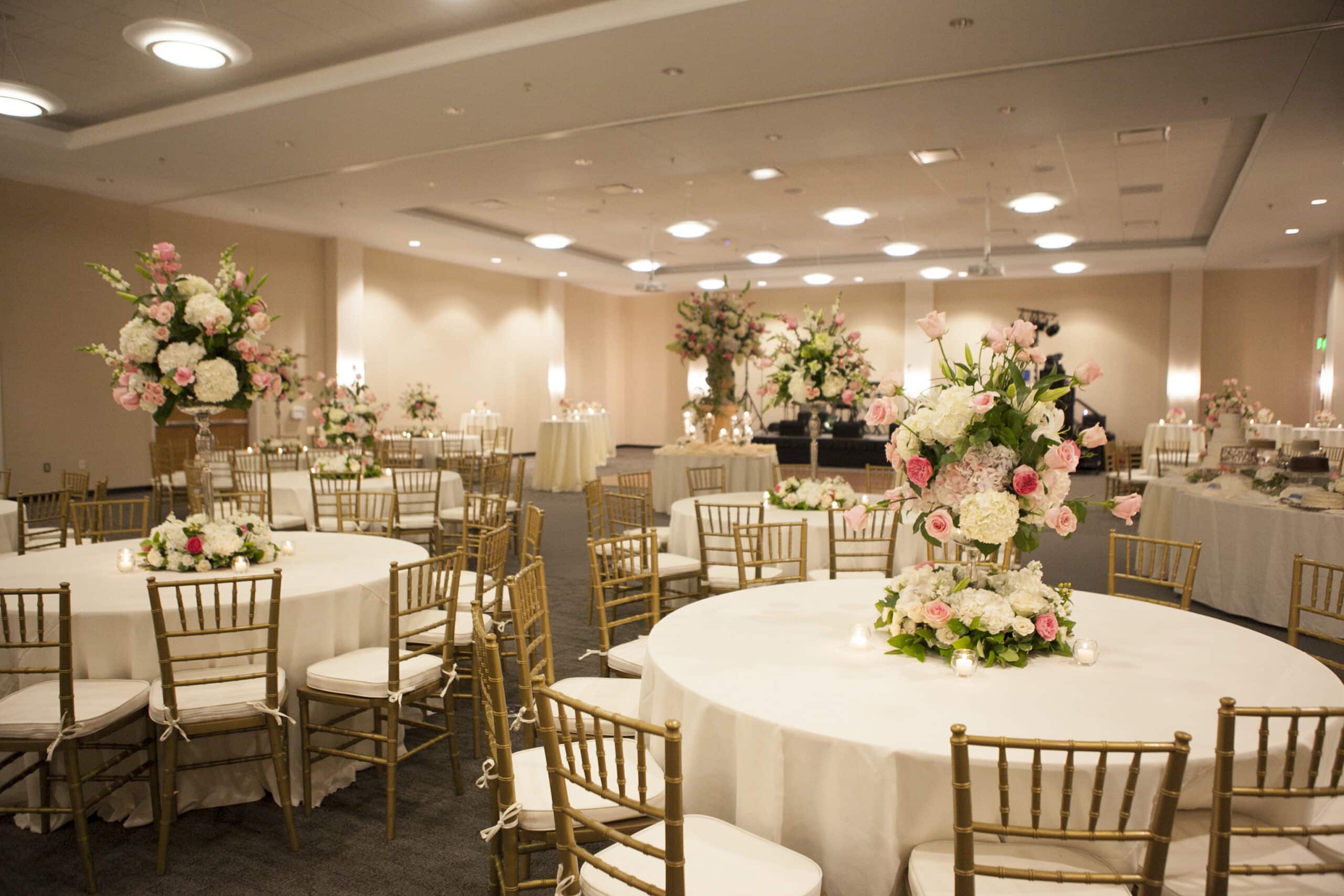 Sandersville's Tarbutton Center set with round tables and gold chairs, featuring large floral centerpieces of pink and white roses.