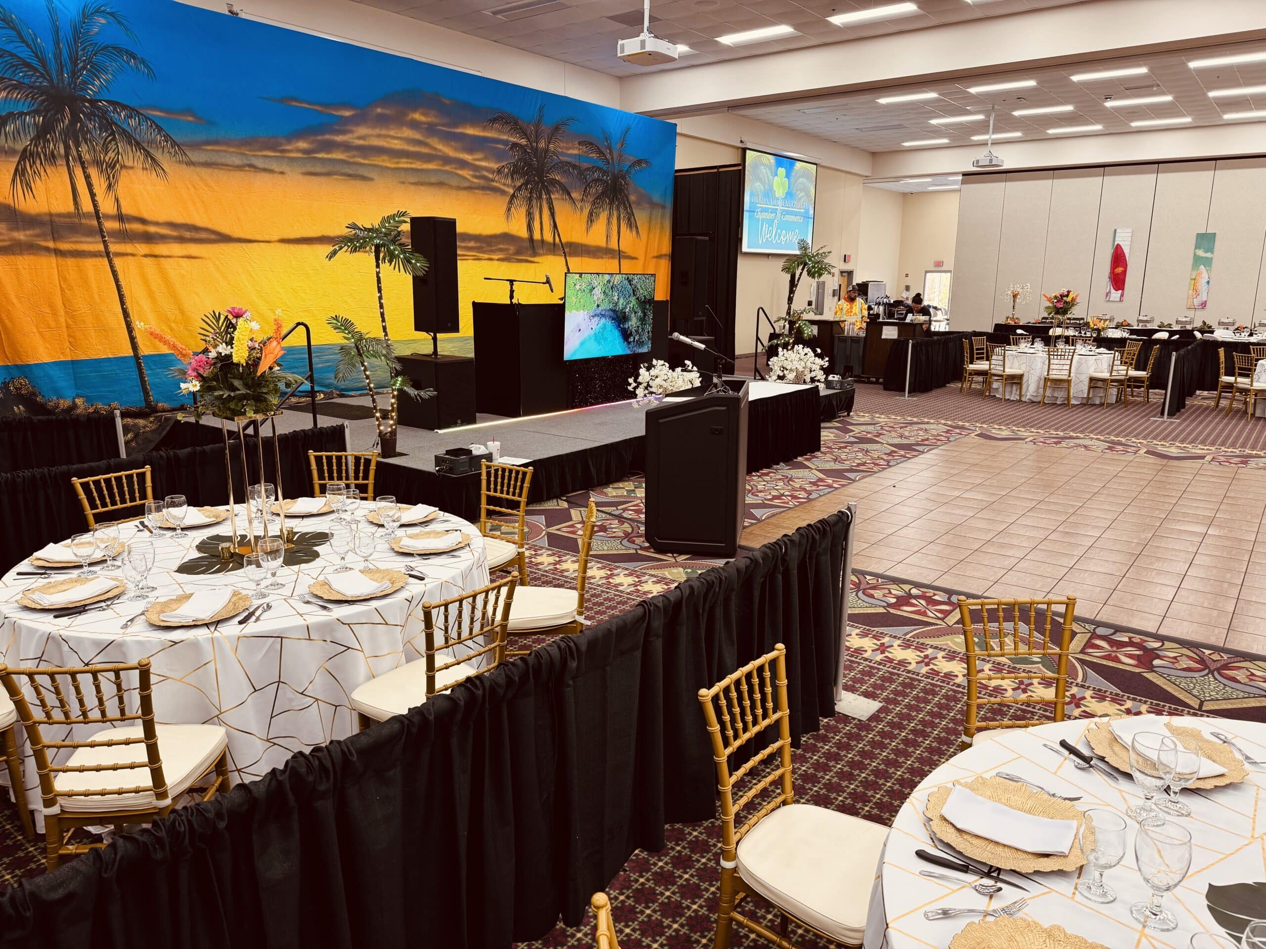 Dublin's Porter Center set for a tropical-themed event with round tables and a stage featuring a sunset backdrop with palm trees.